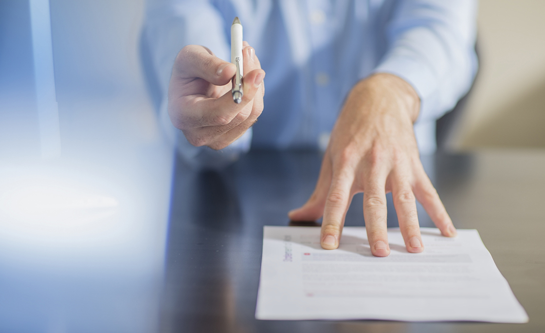 Person sitting at office desk presenting ballpen and contract
