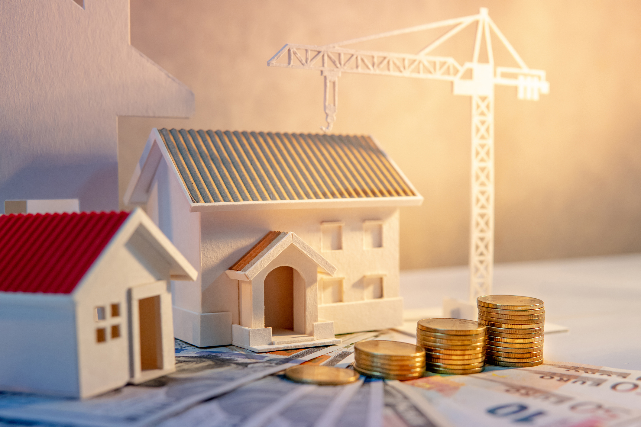 Real estate or property development. Construction business investment concept. Home mortgage loan rate. Coin stack on international banknotes with house and construction crane model on the table.