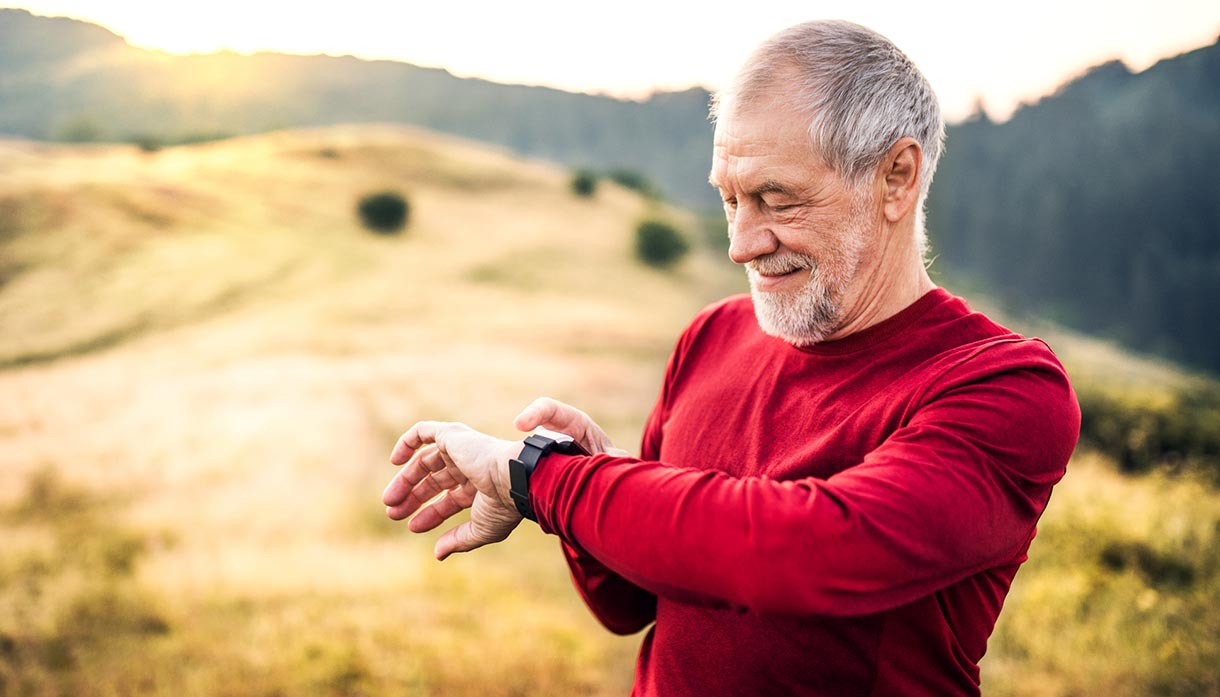 A portrait of an active senior man outdoors in nature at sunrise, checking the time. Copy space.