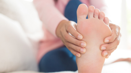 Low Section Of Woman Touching Foot In Pain While Relaxing On Bed