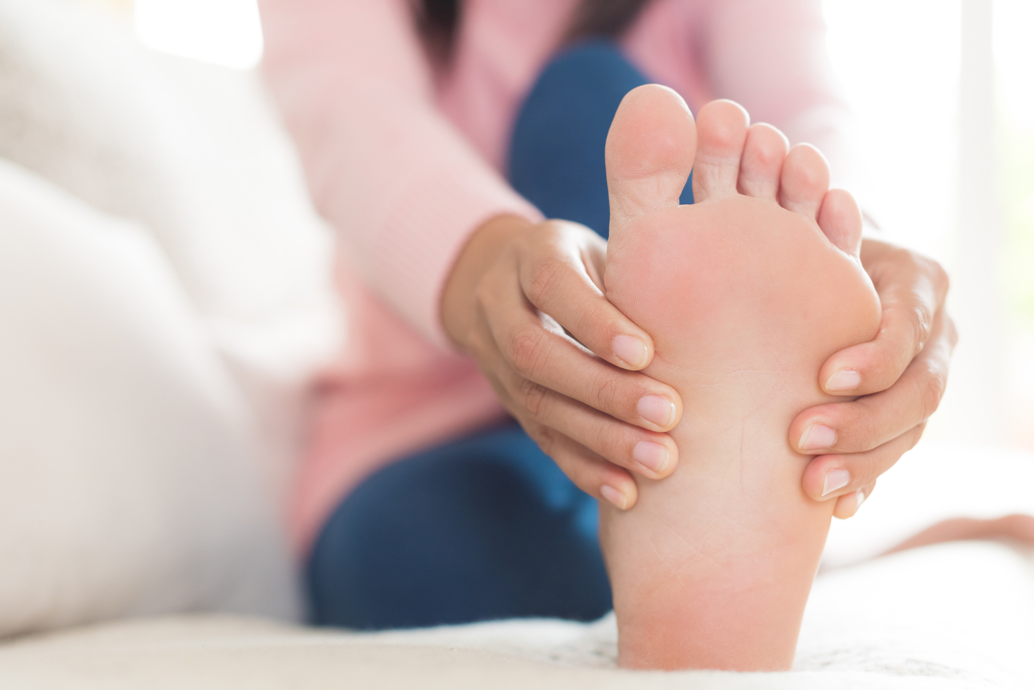 Low Section Of Woman Touching Foot In Pain While Relaxing On Bed