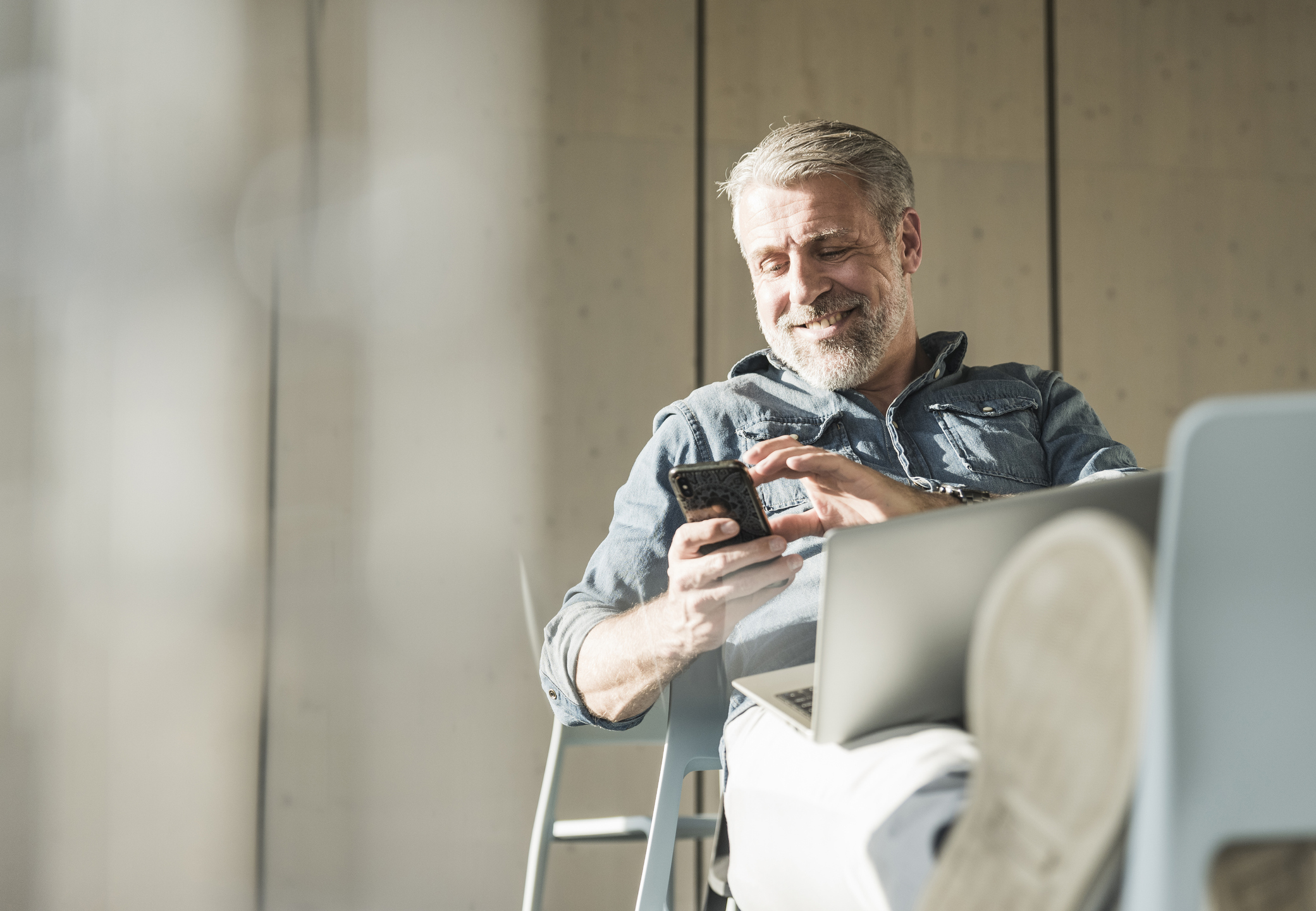 Smiling casual mature businessman with laptop and cell phone