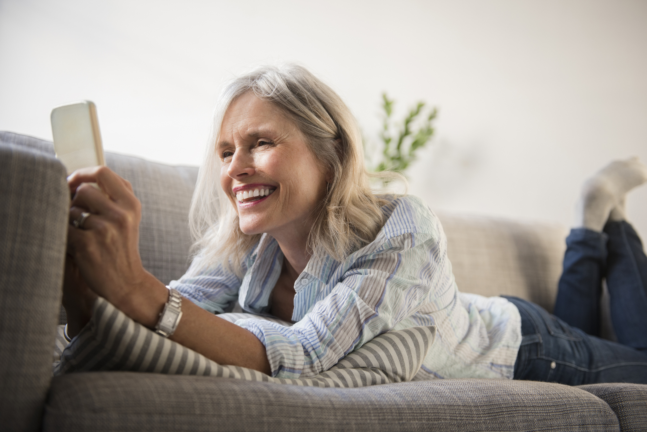 Smiling Caucasian woman laying on sofa texting on cell phone