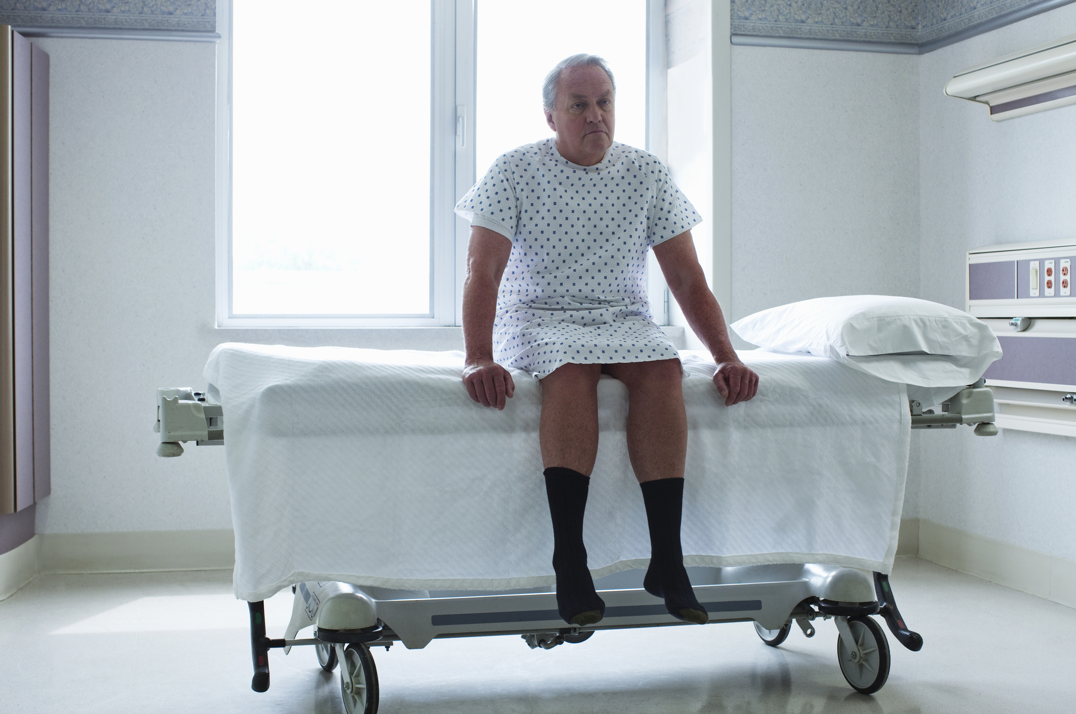 Senior man sitting on bed in hospital room