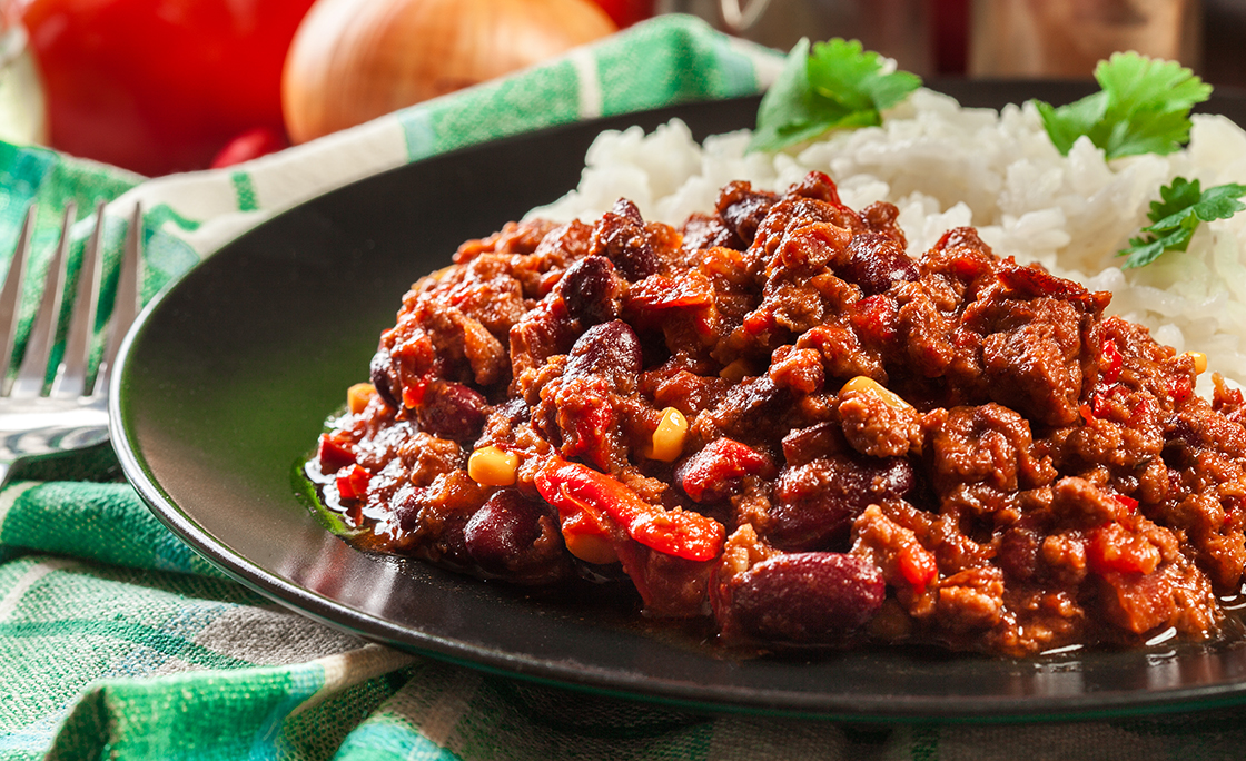 Hot chili con carne with ground beef, beans, tomatoes and corn served with rice