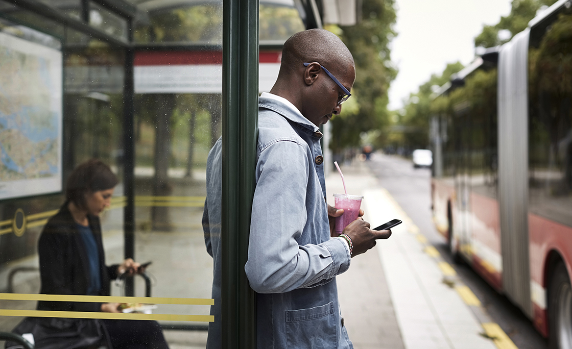 Businessman using smart phone while holding drink at bus stop in city
