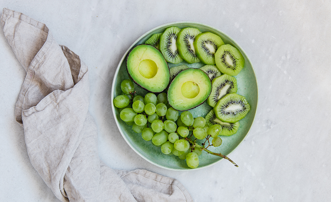 grapes, avocado and kiwi fruit in green rustic plate on marble texture background with copy space