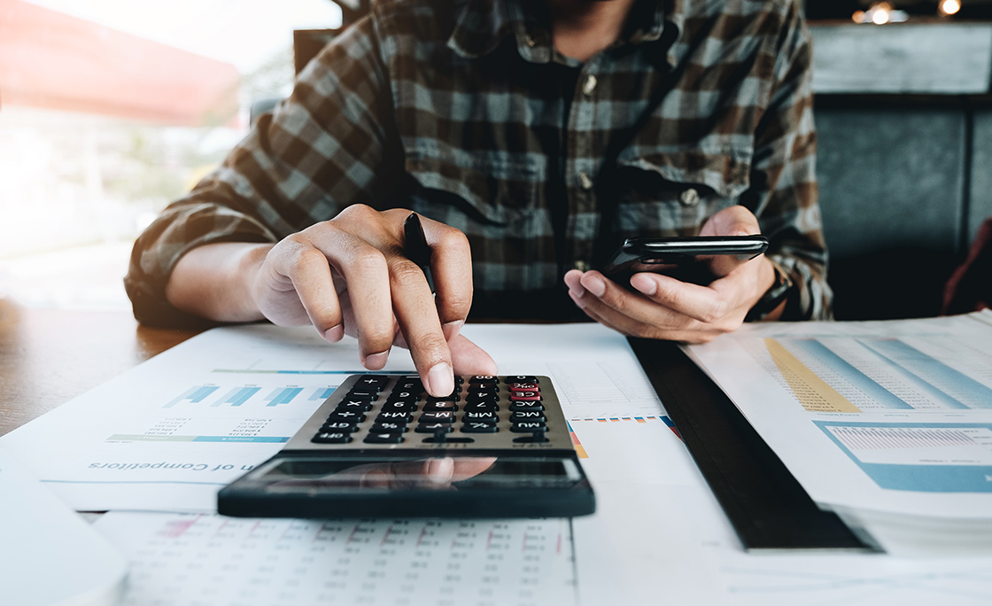 Midsection Of Businessman Using Mobile Phone And Calculator At Desk In Office