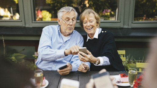 Happy senior couple using mobile phone at outdoor restaurant