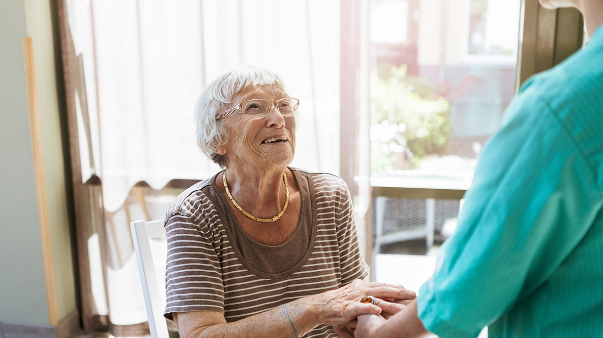 Smiling senior woman holding hands of healthcare worker at nursing home