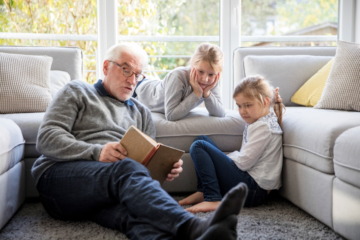 Two girls and grandfather reading book in living room