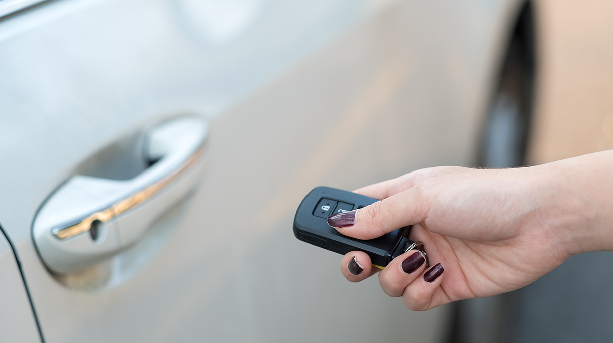 Car remote on hand, pressing button to unlock a car