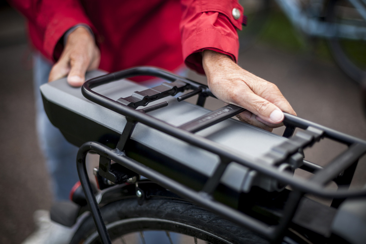 Midsection of senior woman inserting battery in backseat of electric bicycle