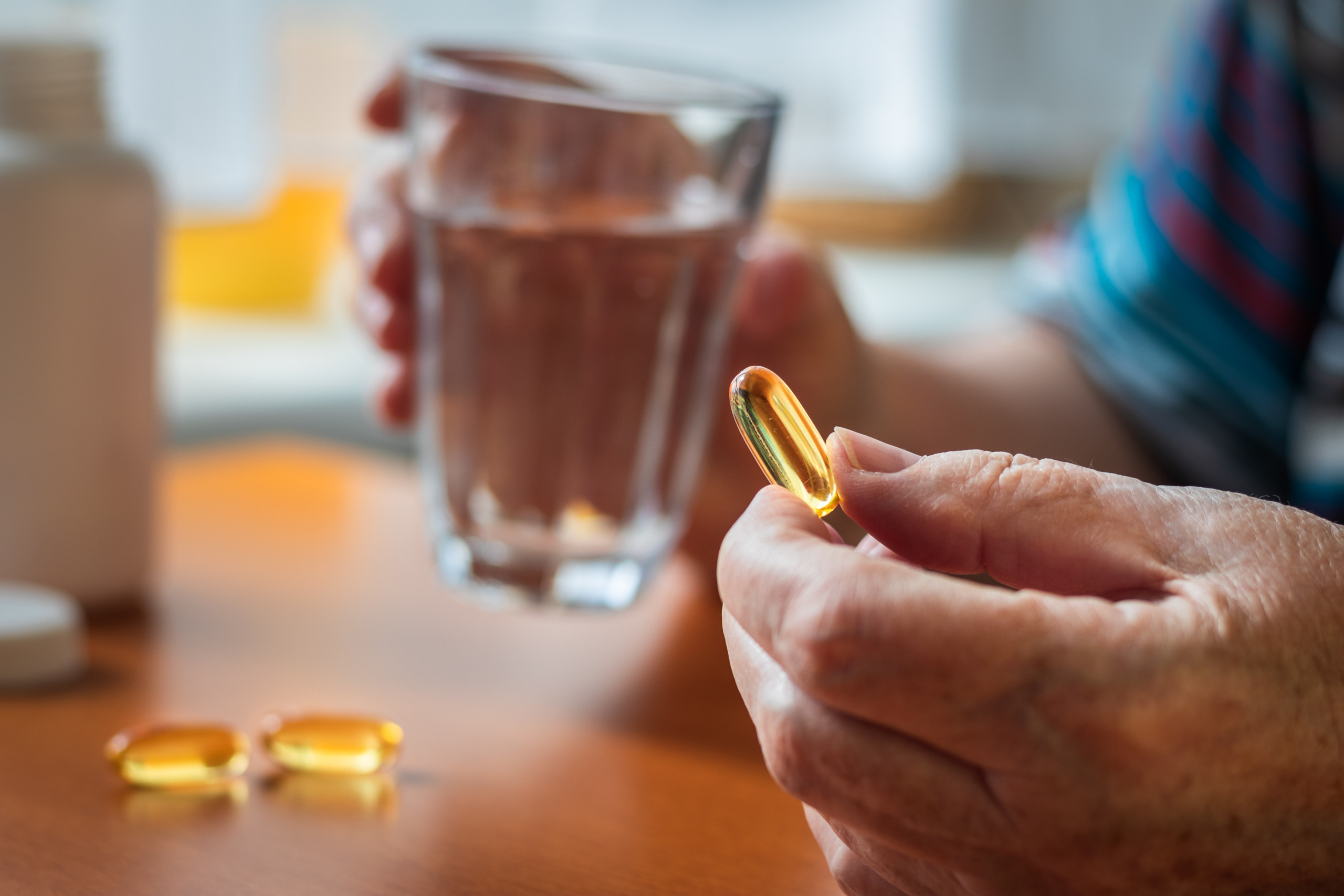 Senior woman holding omega-3 fish oil capsule and glass of water in her hands. Taking food supplement.