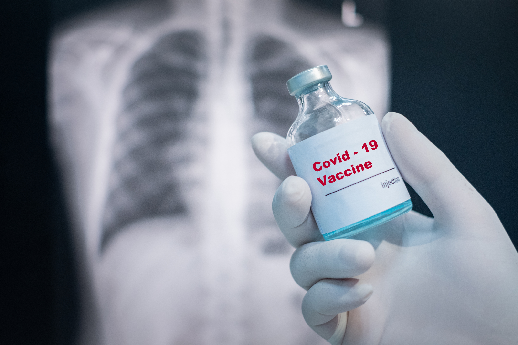 Doctor’s hand holding a covid-19 vaccine vial on Chest x-ray background