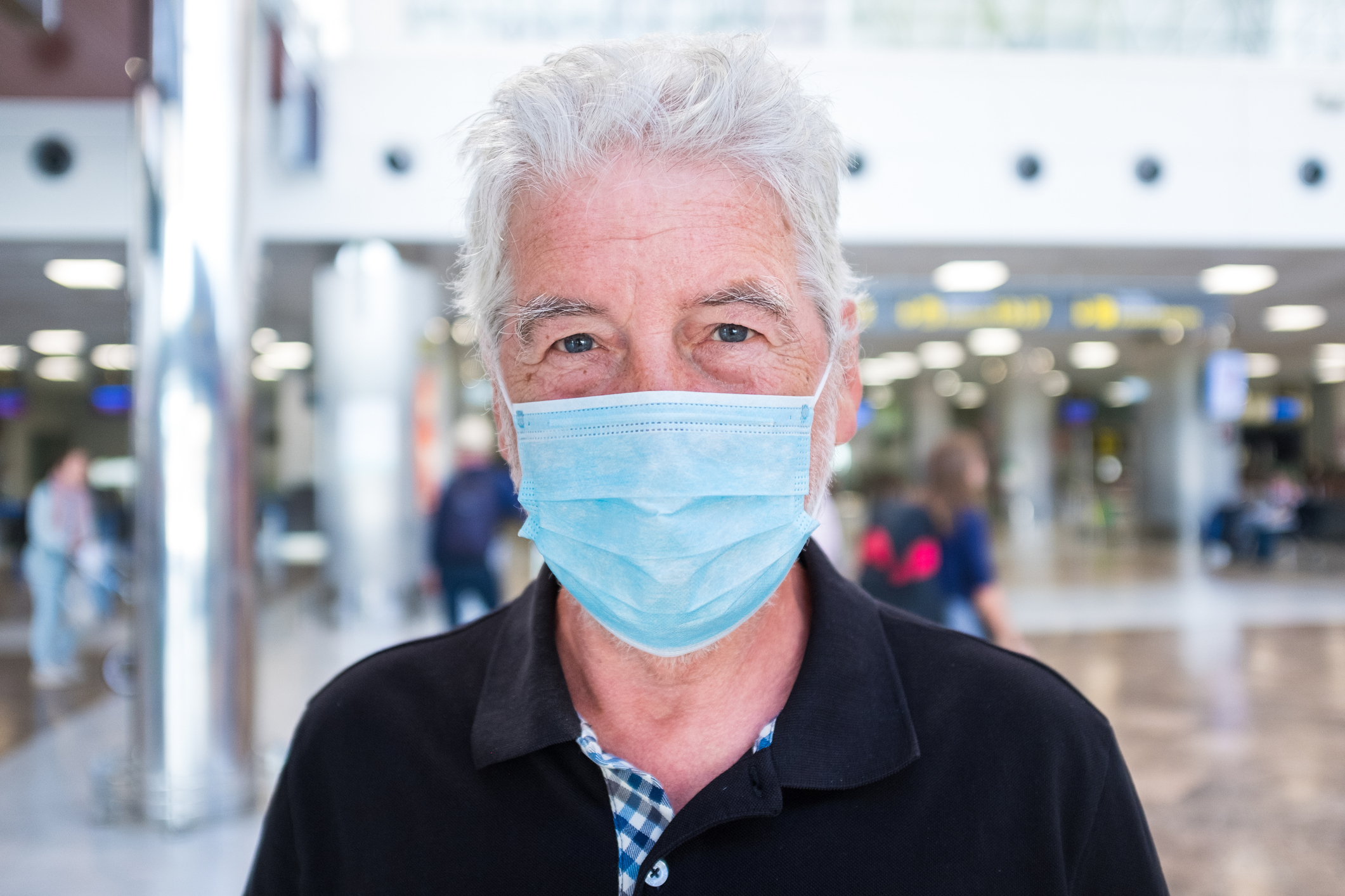 close up and portrait of maturte man and senior looking at the camera seriously worried to travel with the virus in the air ( covid-19 ) – one pensioner at the airport looking at the camera
