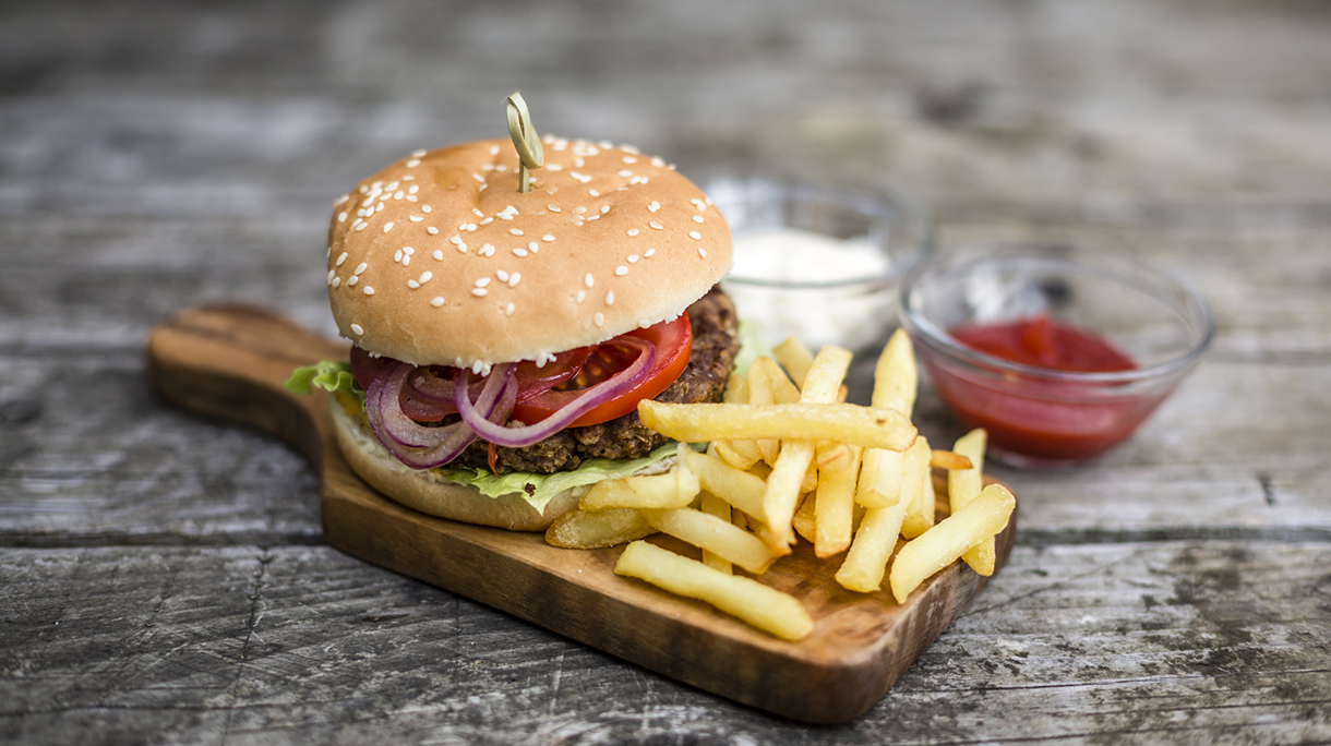 Homemade burger with lettuce, meat, tomato, onion and french fries on chopping board