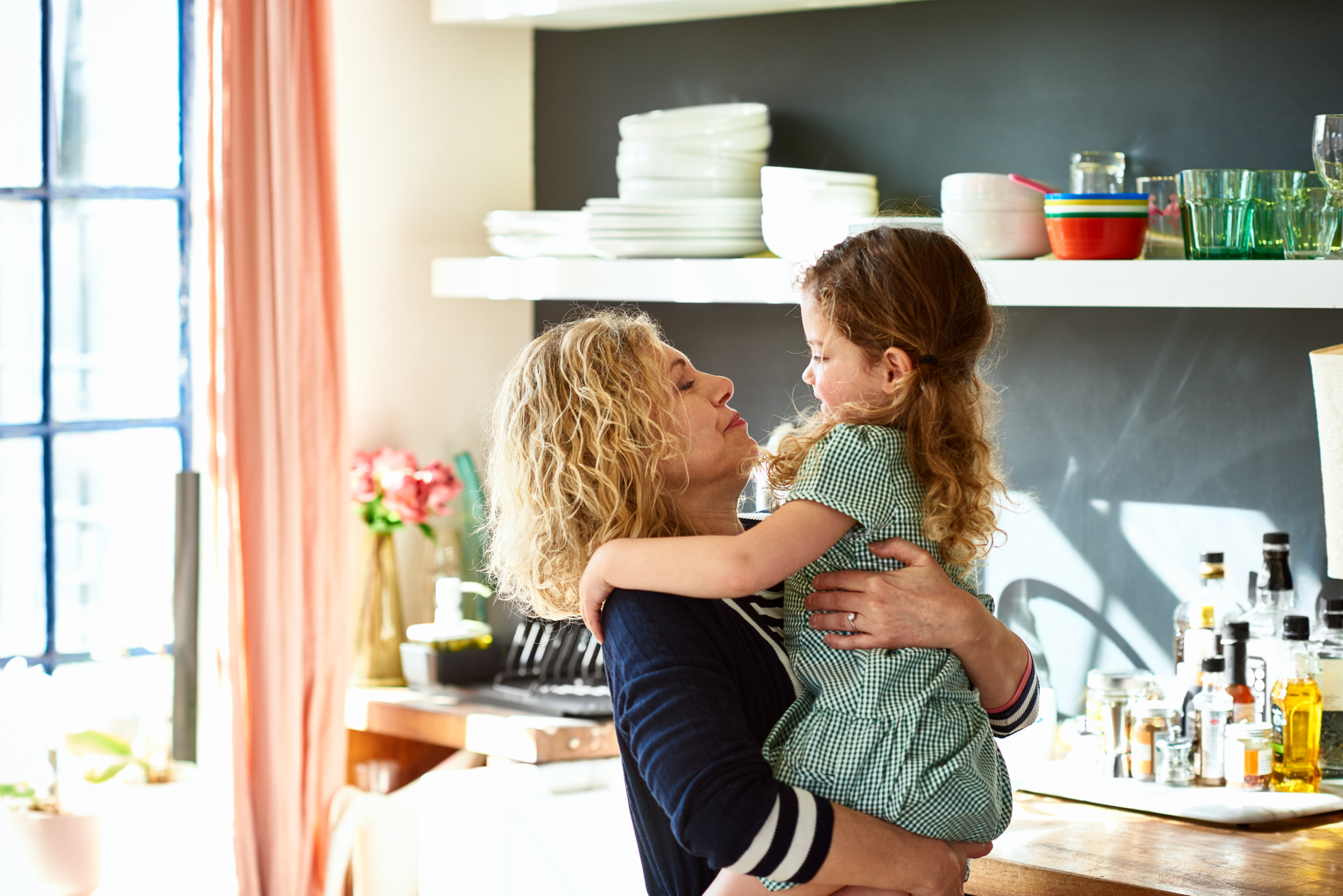 Grandmother hugging little girl in school uniform in kitchen