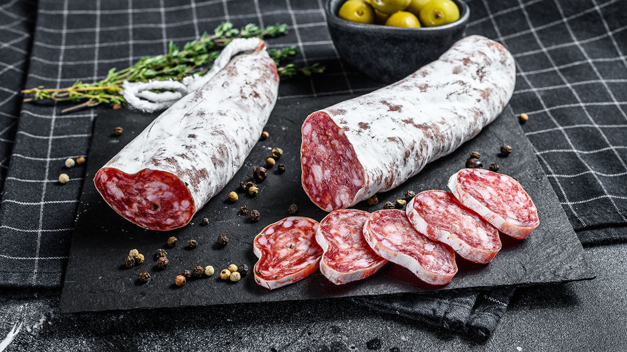 Fuet Salami cut in slices and Rosemary. Traditional Spanish sausage. Black background. Top view