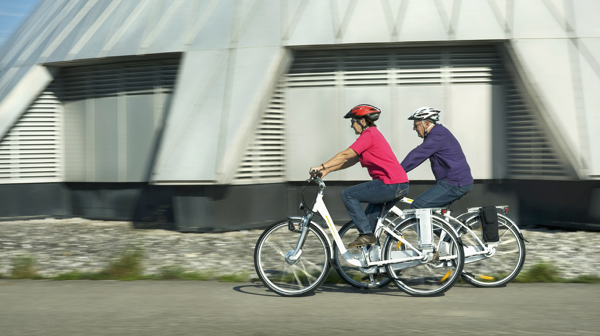 Germany, Bavaria, Raisting, Senior couple riding electric bicycle near radio station