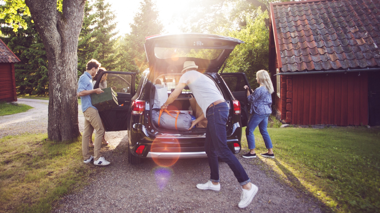 Full length of friends loading luggage into car on road during sunny day