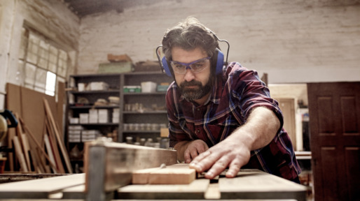 Carpentry business owner cutting a plank of wood in workshop