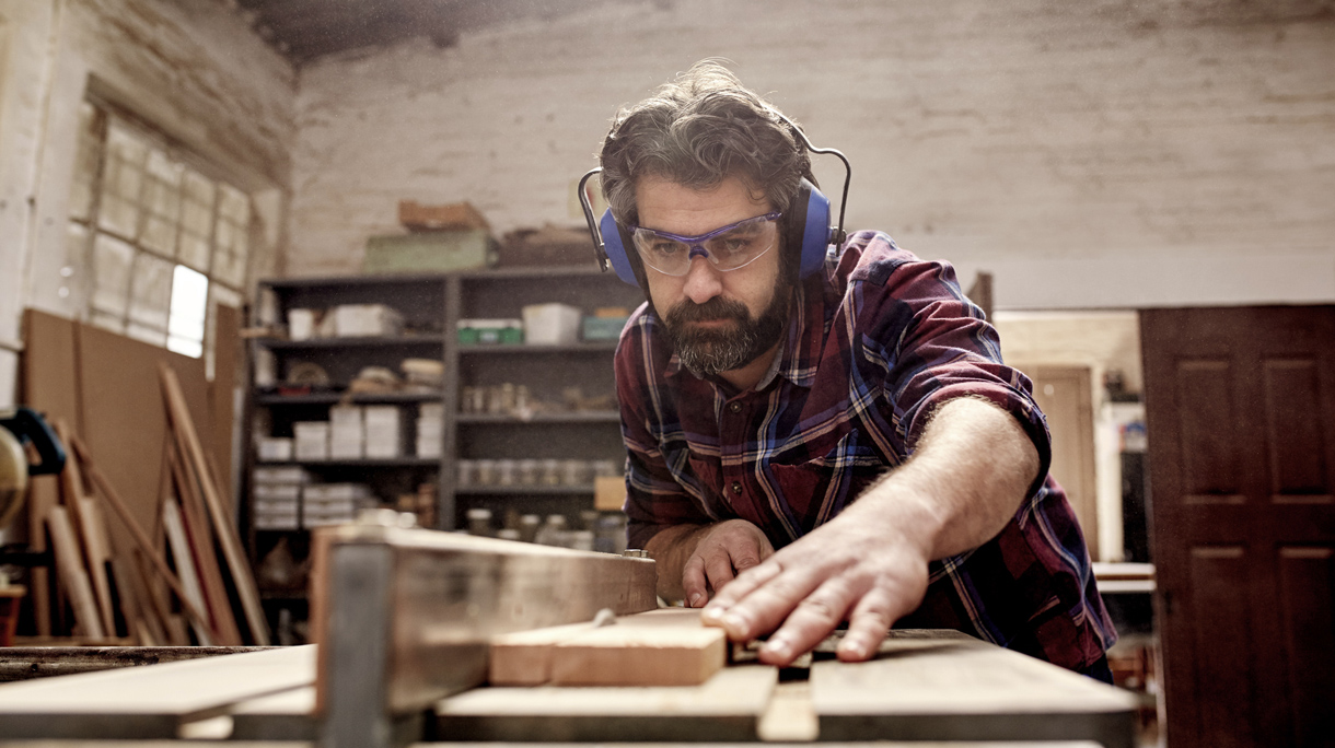 Carpentry business owner cutting a plank of wood in workshop