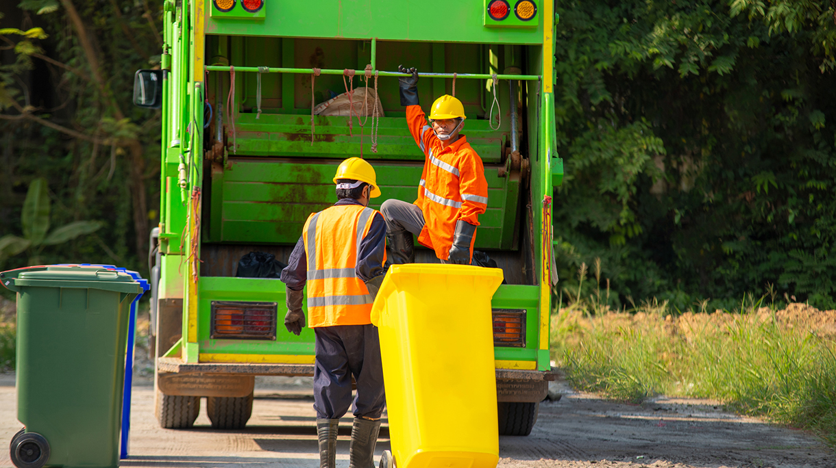 Two garbage men working together on emptying dustbins for trash removal.
