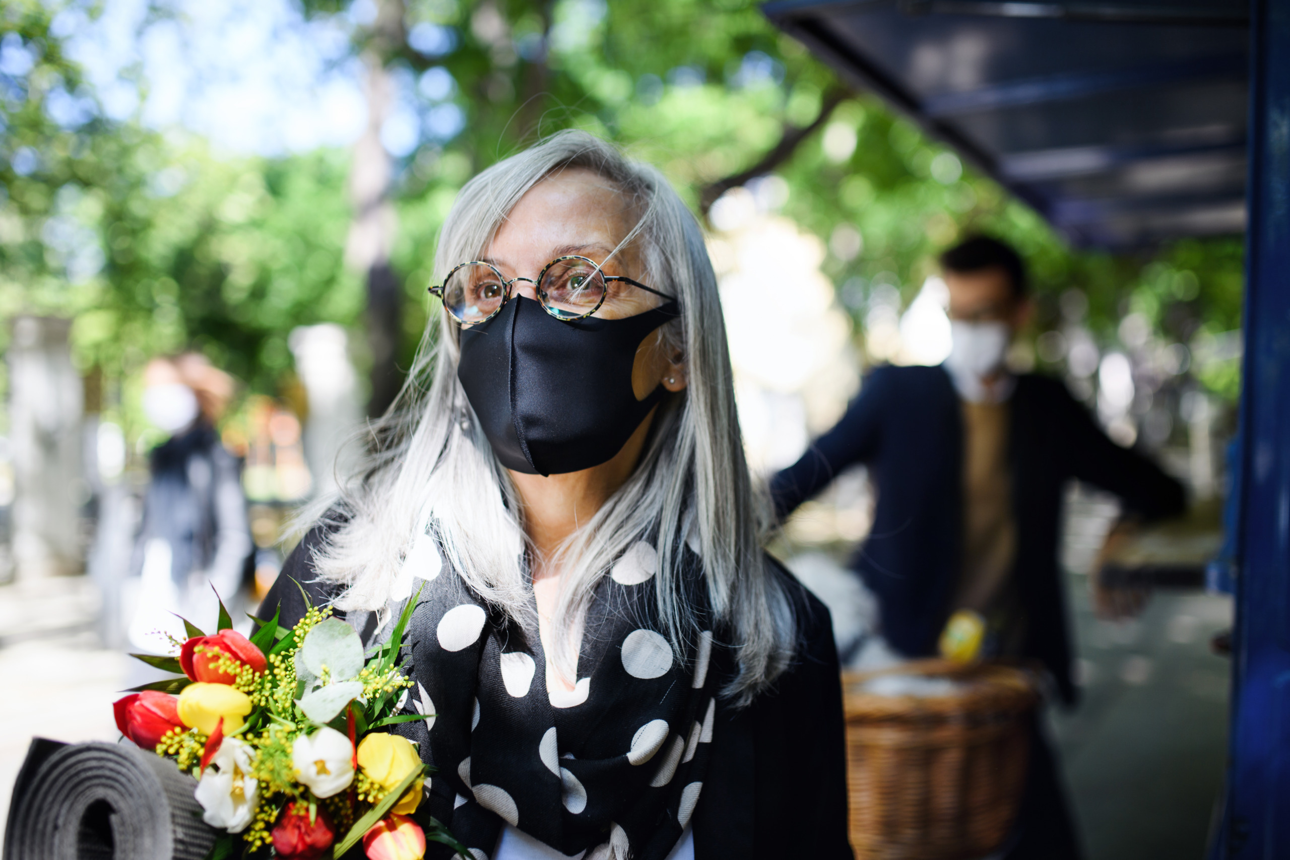 Portrait of senior woman with face mask and exercise mat walking outdoors in city.