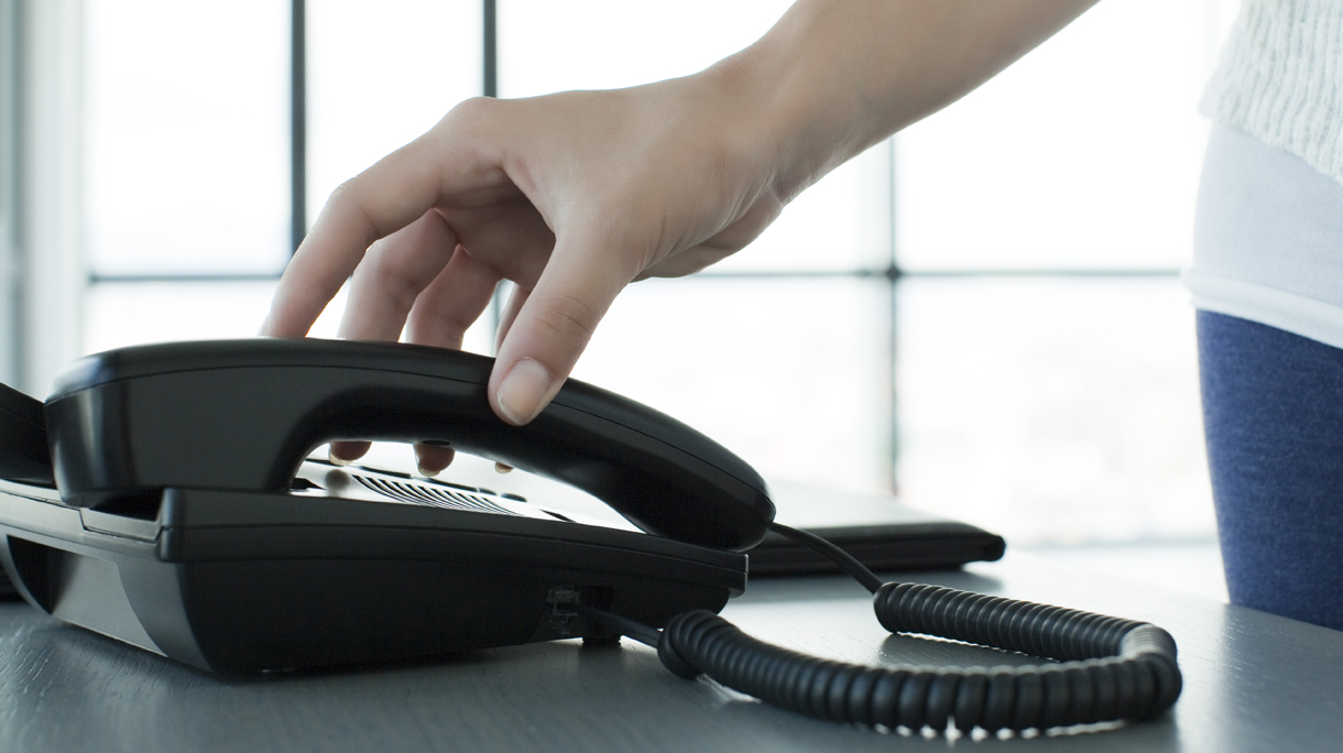 Woman picking up telephone receiver, backlit, cropped