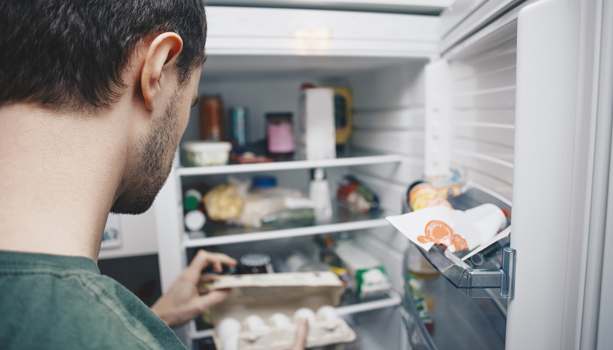 Man holding egg carton by refrigerator in kitchen