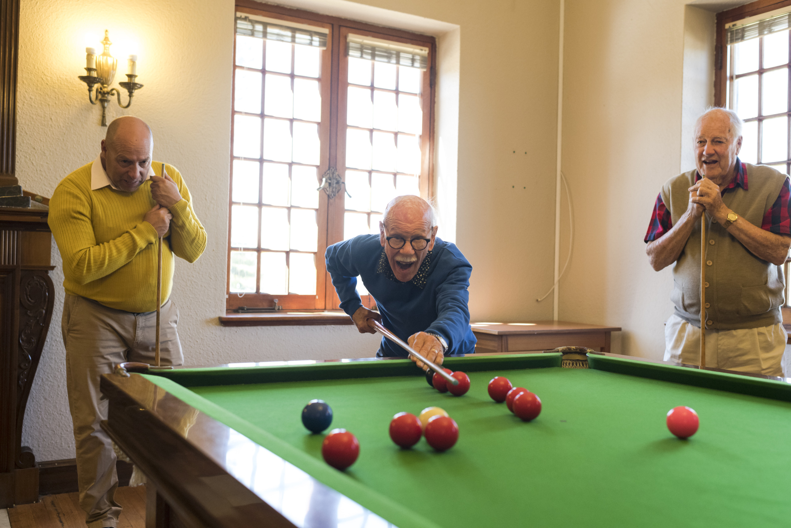 90+ year old senior man confidently showing his skills in snooker to friends