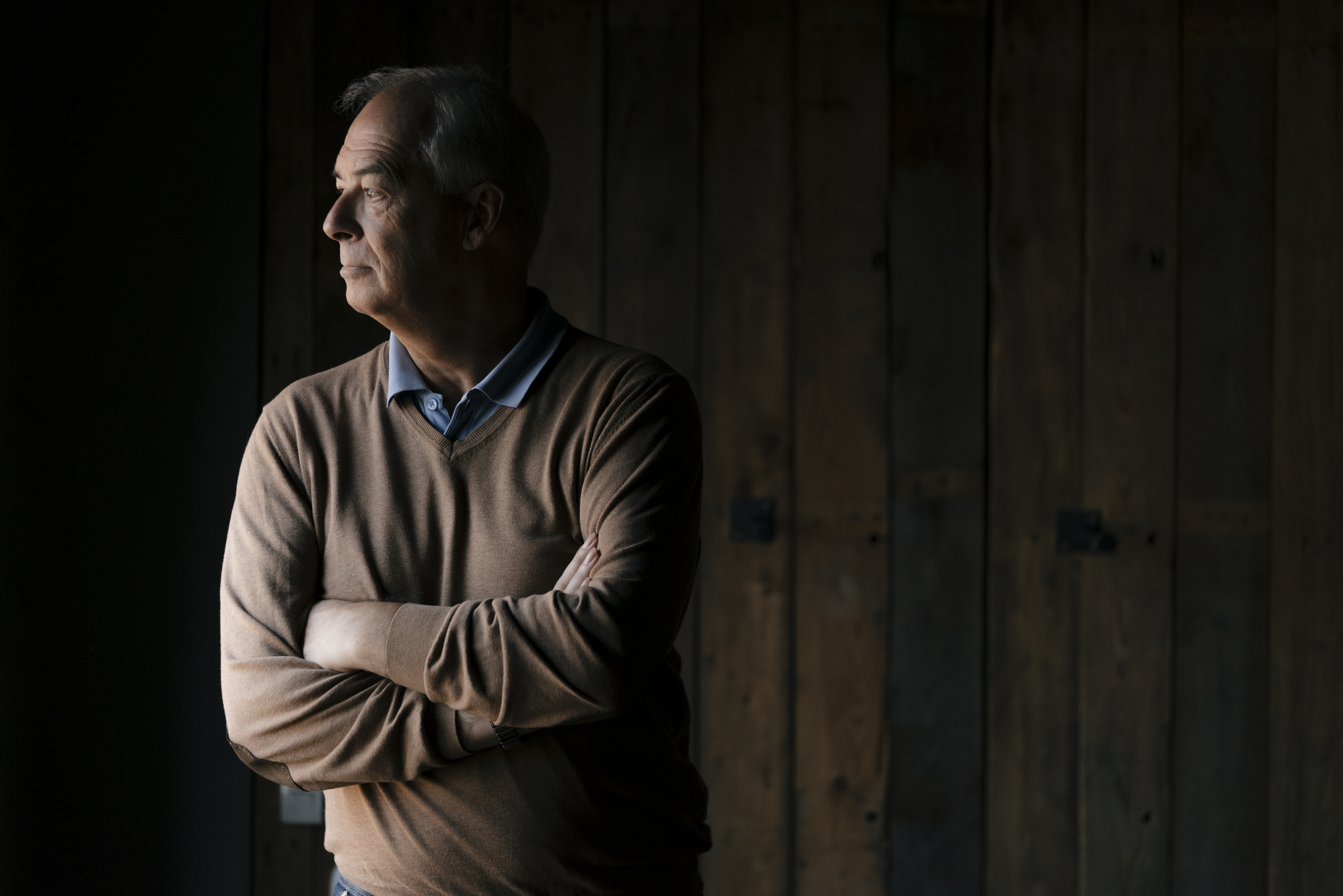 Serious senior businessman in front of wooden wall looking sideways