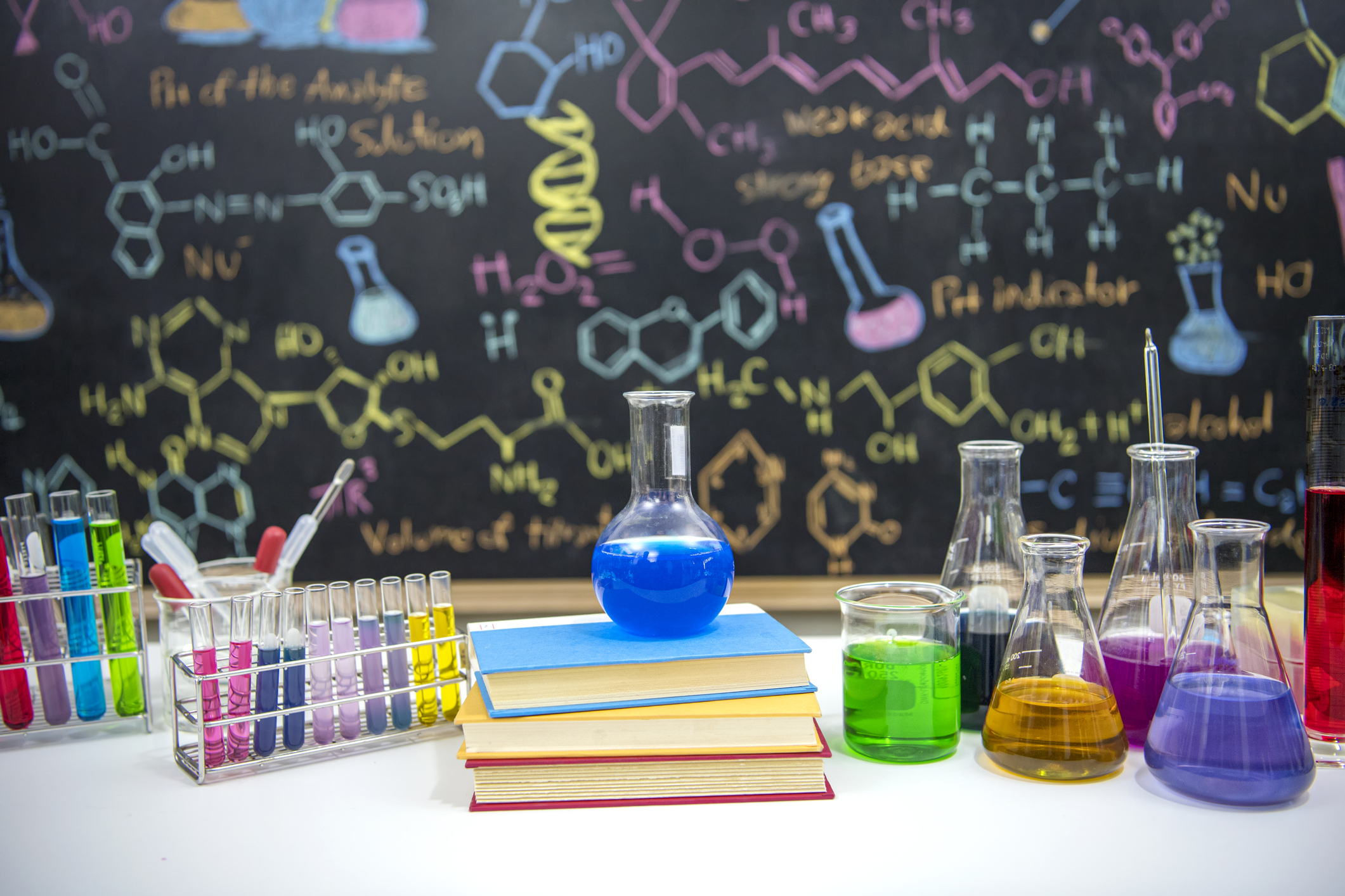 Classroom desk and drawn formula on blackboard of chemistry teaching with books and instruments.