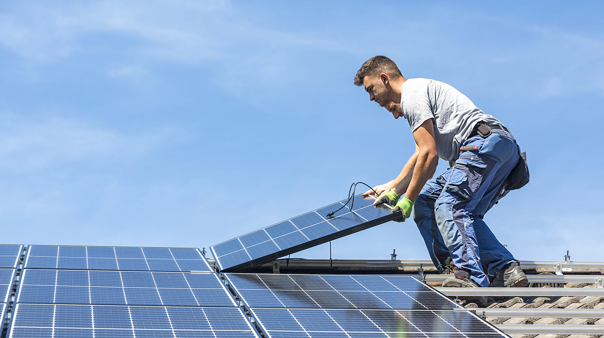 Men Holding Solar Panel While Standing On Roof Against Sky