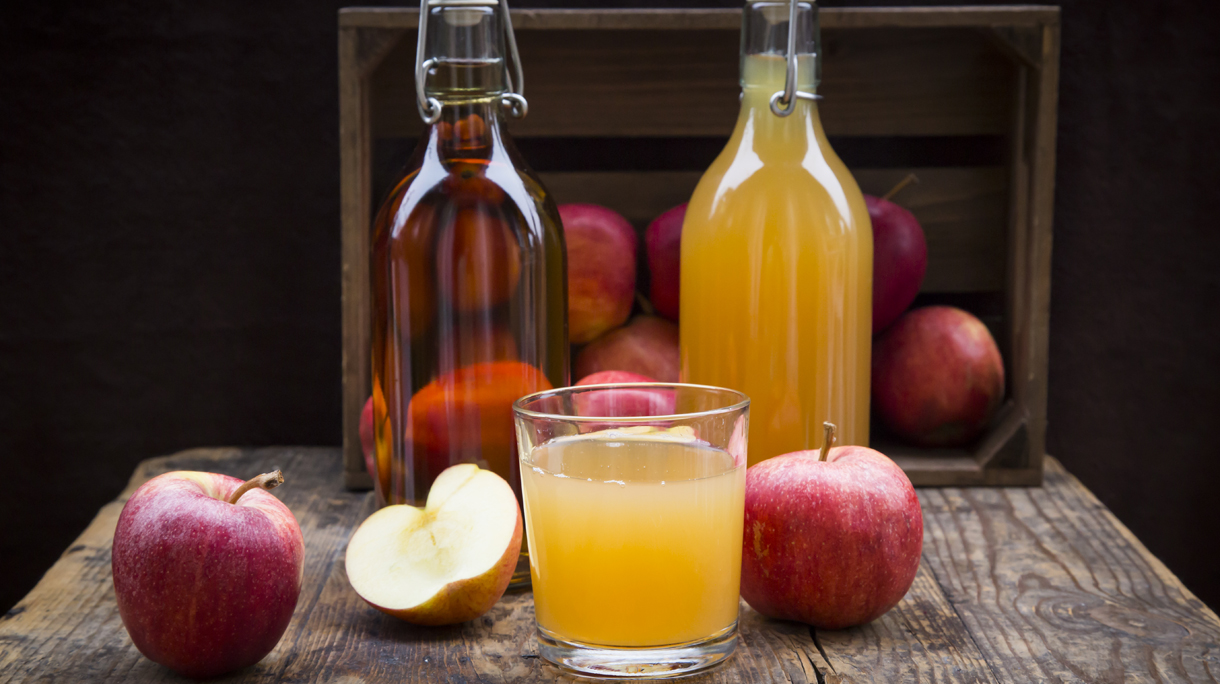Bottle and glass of apple juice, cloudy and clear, red apples on wood
