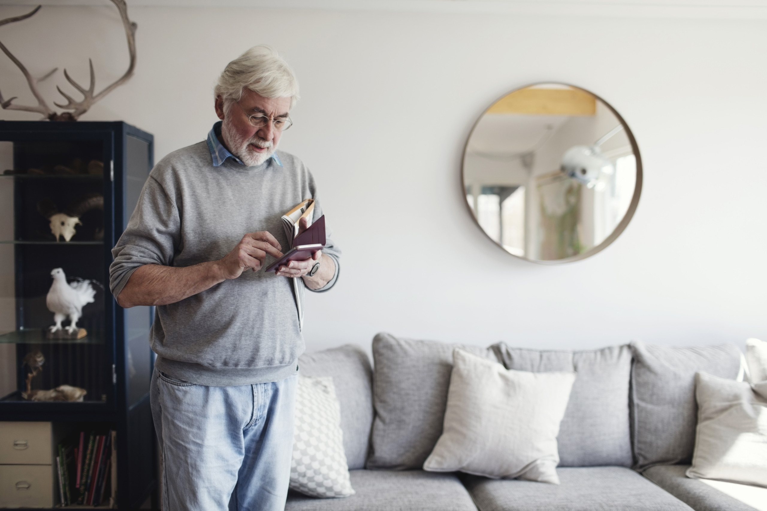 Senior man using mobile phone while standing by sofa at home