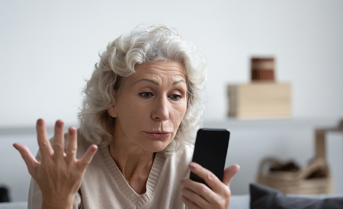 Grandmother holding smartphone looks at device screen feels angry