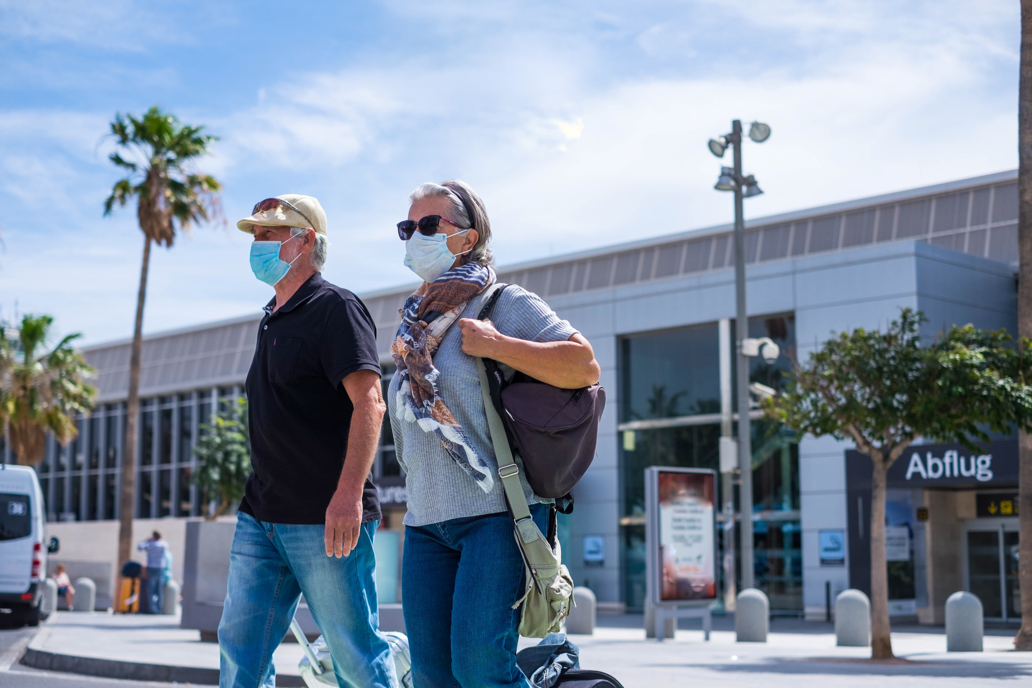 two senior walking with their baggage and wearing medical mask to prevent covid-19 or coronavirus or another type of virus or disease – safe travelers concept and lifestyle walking outdoor