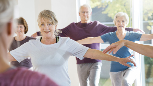 Seniors following teacher in yoga exercise class.