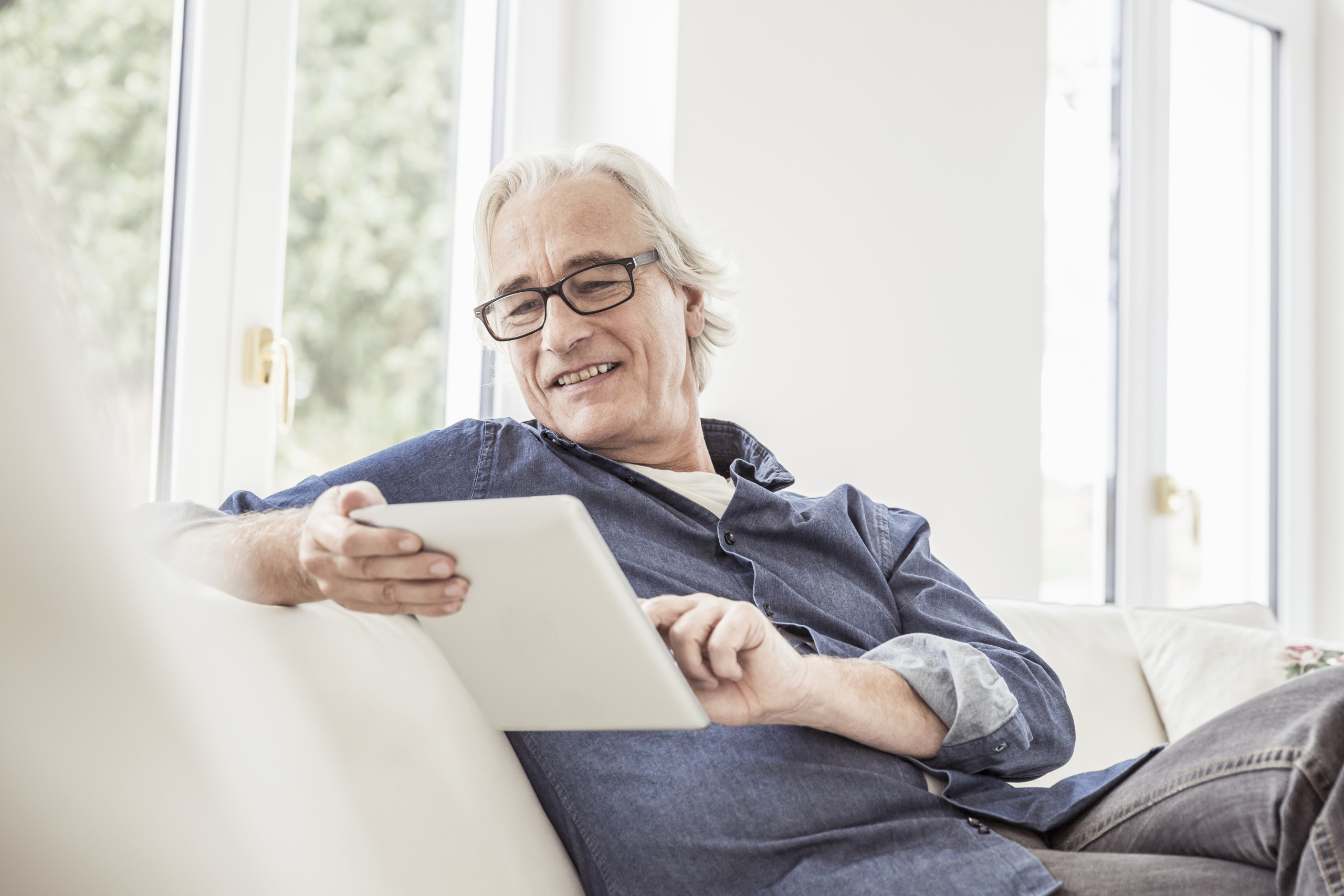 Senior man sitting on sofa, using digital tablet