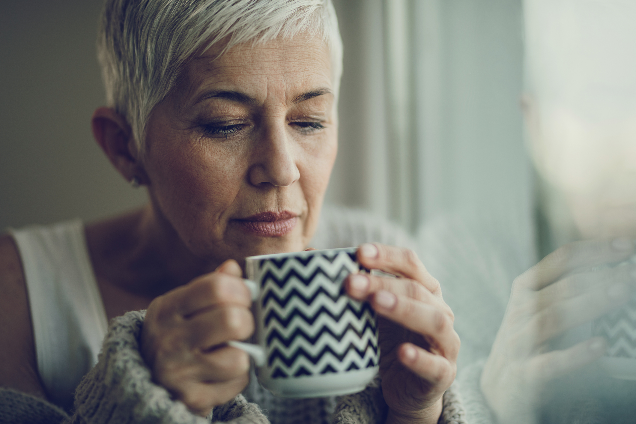 Portrait of a senior woman with coffee cup by the window.