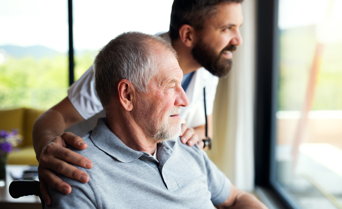 A male healthcare worker talking to senior man in wheelchair indoors at home.