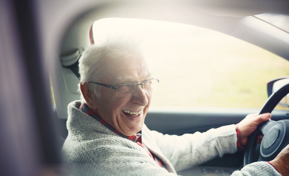 Old gentleman drives car and laughs at the camera