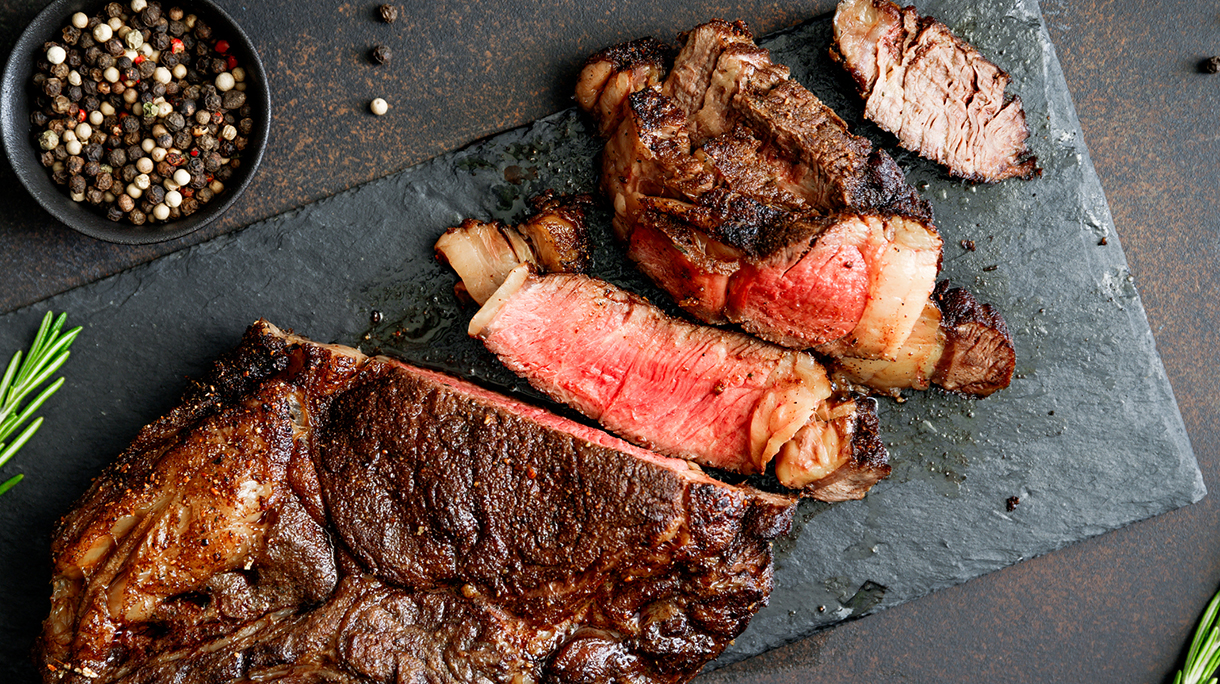 Top view of dry-aged marble beef steak Tomahawk on black slate with spices. Flat lay, dinner concept.