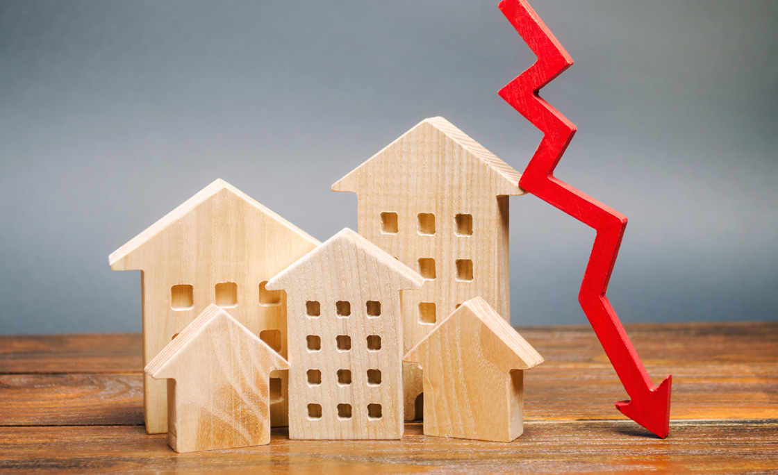 Miniature wooden houses and a red arrow down. The concept of low cost real estate. Lower mortgage interest rates. Falling prices for rental housing and apartments. Reducing demand for home buying