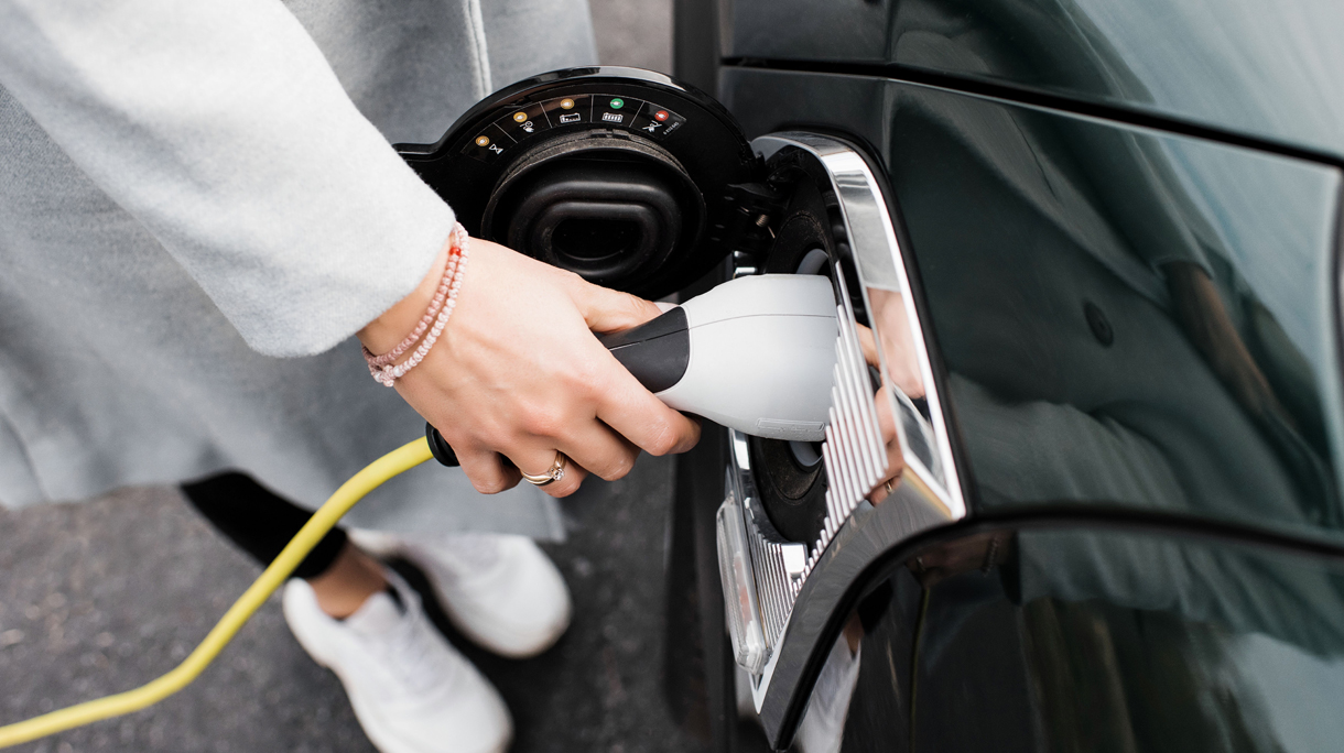 woman’s hand plugging in a charging lead to her electric car