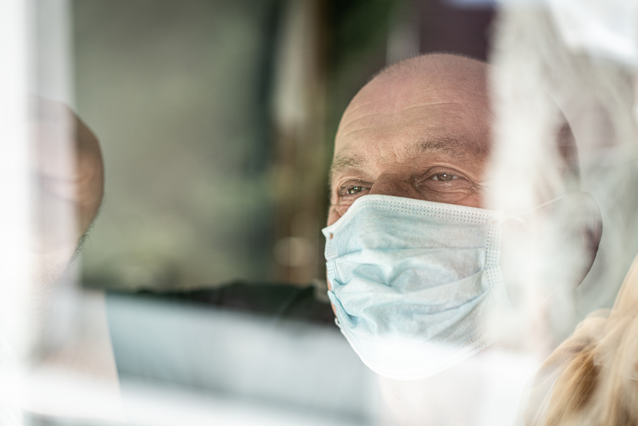 Senior man with mask looking trough window
