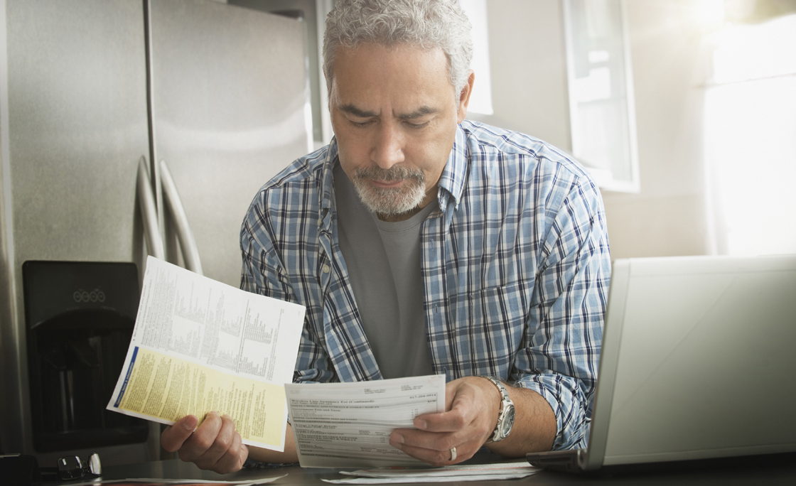 Hispanic man paying bills on laptop in kitchen