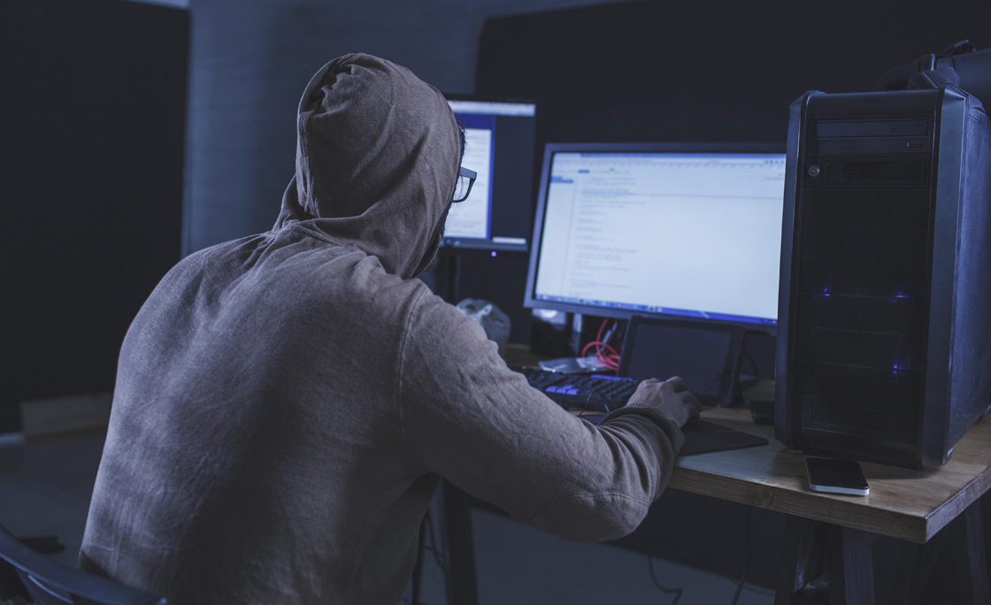 Computer hacker wearing hooded shirt using computer at table